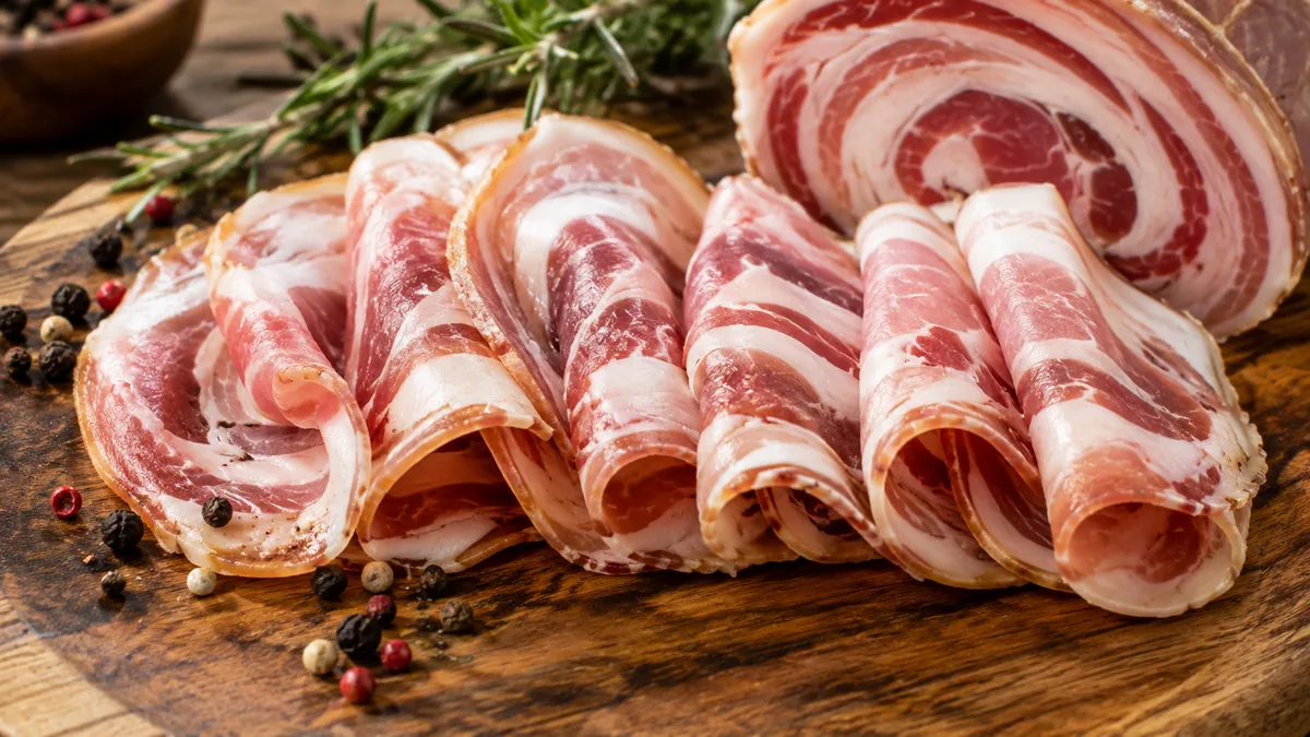 Tranches fines de pancetta italienne roulée sur planche en bois